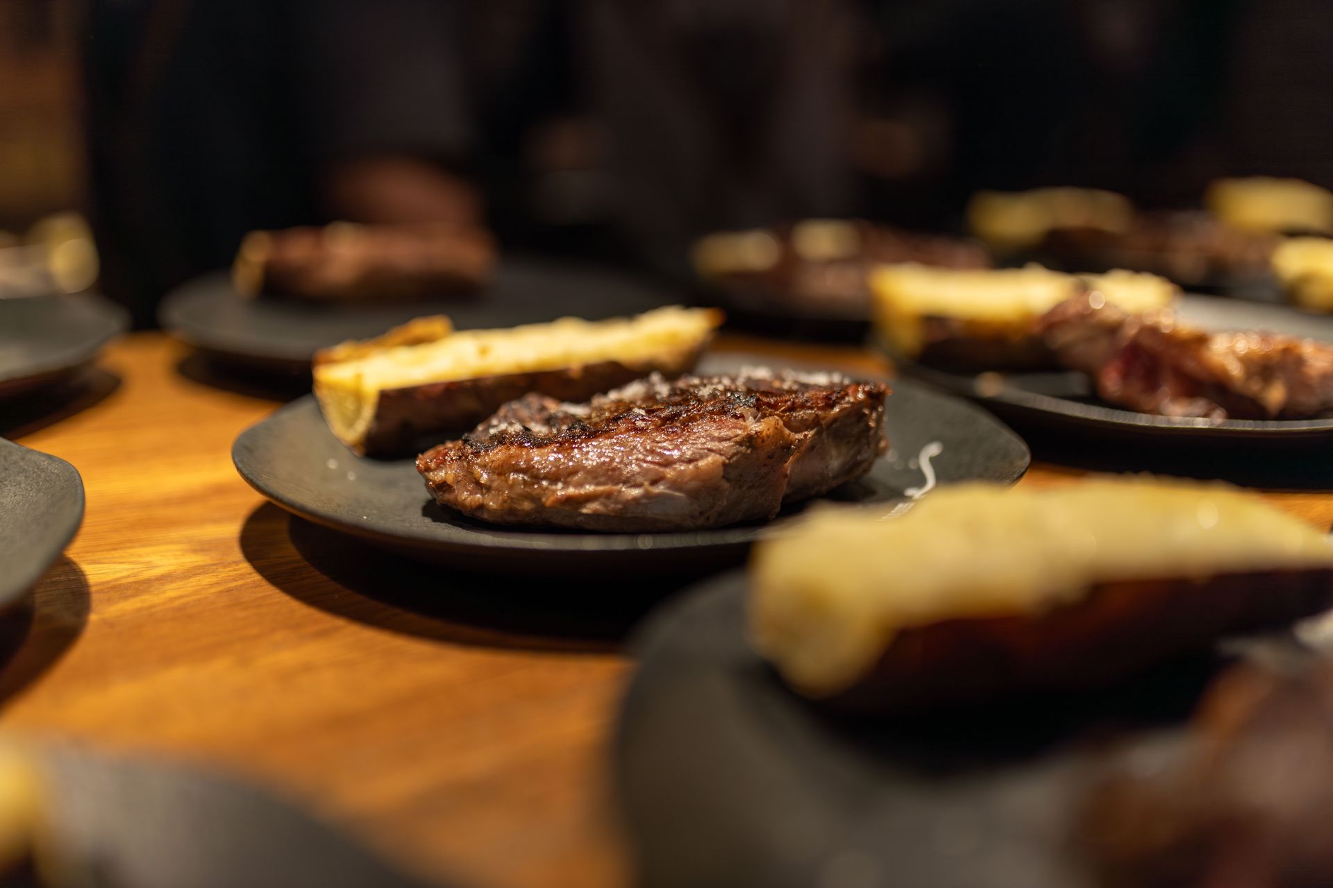 Close-up of a succulent grilled steak served indoors with roasted sides on black plates.